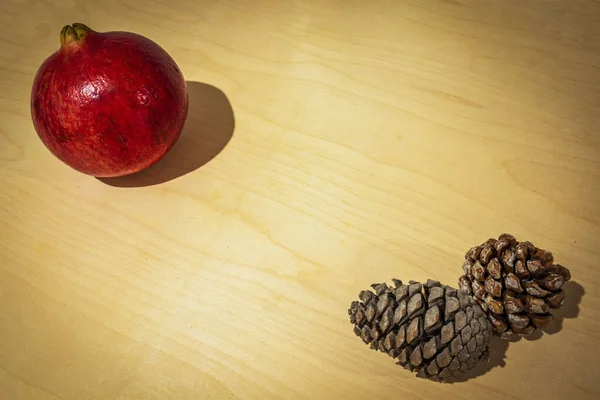 winter fruit on a wooden floor. Red pomegranate and pine cones. Christmas and winter holidays.