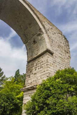 Narni, Terni, Umbria 'daki Augustus' un Roma kemer köprüsünün kalıntıları. Nera Nehri üzerindeki köprünün kalıntıları. Büyük ve antik taş kemer, mavi gökyüzüne karşı. Ağaçlar ve yoğun bitki örtüsü