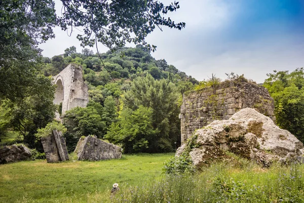 An artist paints live the ruins of the Roman arch bridge of Augustus, in Narni, Terni, Umbria. Plein air painting, impressionism. The remains of the bridge over the Nera river, surrounded by nature.