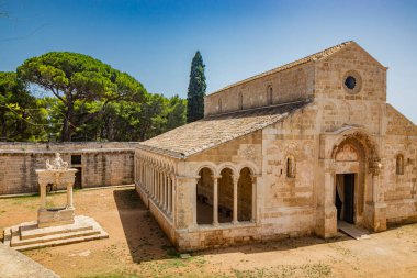 10 Ağustos 2021 - Santa Maria Manastırı a Cerrate, Puglia, Salento, Lecce - Antik Roma Kilisesi, FAI 'nin mirası. Ön cephe, kuyu ve sütunları olan kapıcı. Yazın mavi gökyüzü.