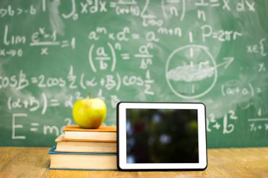 Dijital tablet ve kitap yığını üzerinde elma
