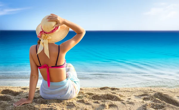 Ung kvinde nyder solen sidder på en strand tæt på havet - Stock-foto