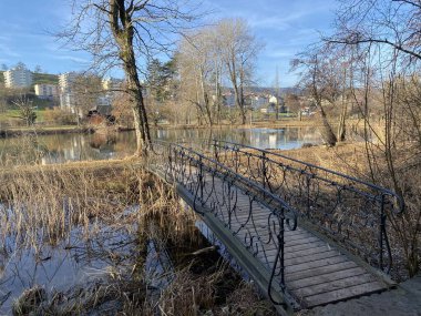 A small pedestrian bridge next to Au Castle with the surrounding park and on Lake Au (Ausee), Wadenswil (Waedenswil) - Canton of Zurich (Zuerich), Switzerland / Schweiz