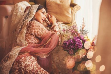 Muhteşem klasik Hint gelini lüks bir otel odasında geleneksel lehenga ve ghungat giyerek oturuyor.
