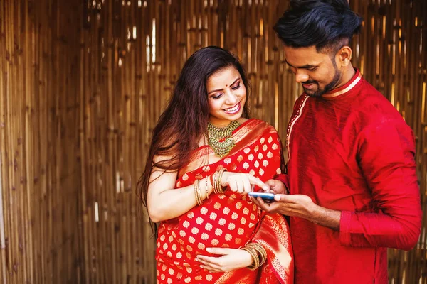 快乐的印度孕妇和丈夫在网上选择医生 快乐的夫妻一起用电话 图库图片