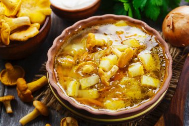 Seramik tabakta chanterelles çorbası ve ahşap bir masada taze mantar.