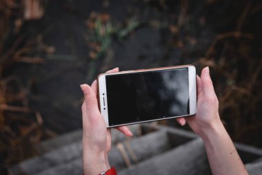 Kadın telefonu büyük siyah ekranlı ve kırmızı spor bantlı kullanıyor. Açık hava, karanlık sonbahar tonları, mobil ve internet iletişim kavramı