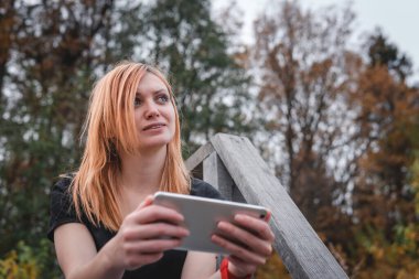 Akıllı telefon kullanarak gülümseyen mutlu kadın. Doğa yürüyüşü. Orman geçmişi. Sonbahar günü. İletişim, internet ve mobil ağ. Boşluğu kopyala