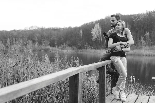 A couple on the old wooden bridge at a lake on autumn day in park. Forest on background. Happy togather, copy space for text. romantic moment, relationship, hiking, outdoor. comfort, black and white