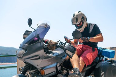 Bisikletçi turistik motosikletiyle akıllı telefon kullanıyor. Gideceğiniz yere varın. Sunny Beach İtalya. Seyahat ve tatil, motosikletçi. Aktif yaşam tarzı. Ağ bir navigasyon sistemi