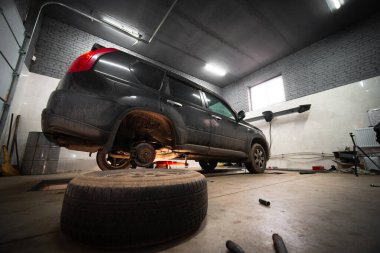 Ön planda yerde bir tekerlek var. Arkada bir araba var. Hizmet ve bakım konsepti. Planlı ve ani. Fren yastıklarının değiştirilmesi. Seçici odak