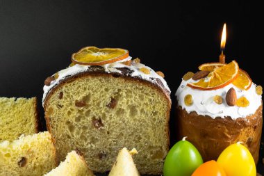 Siyah arka planda geleneksel Paskalya pastası. Göçmen, şekerli meyve, kuru üzüm, dekoratif renkli yumurta, mumlar yanıyor. Bölgesel görüş, dilimler, parçalar. Ortodoks muamelesi.