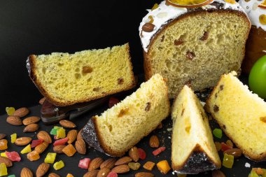 Siyah arka planda geleneksel Paskalya pastası. Göçmen, şekerli meyve, kuru üzüm, dekoratif renkli yumurta. Bölgesel görüş, dilimler, parçalar. Ortodoks muamelesi. Yakın plan.