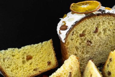 Siyah arka planda geleneksel Paskalya pastası. Göçmen, şekerli meyve, kuru üzüm, dekoratif renkli yumurta. Bölgesel görüş, dilimler, parçalar. Ortodoks muamelesi. Yakın plan.