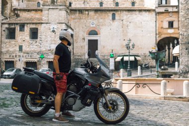 Beyaz kasklı yakışıklı adam eski macera motosikletinin üzerinde oturuyor. Seyahat ve tatil konsepti. Özgürlük için. Narni, İtalya