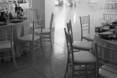 Masa ve şarap kadehli sandalyeler, tabaklar dolu. Peçete ve çatal bıçak takımı. Az ışık. Seçici odaklanma. Partiye hazır, kutlayalım. Restoran hizmetleri, kamu yemek şirketleri. Siyah ve beyaz.