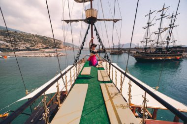 Akdeniz 'in sularındaki eski korsan gemisinde poz veren mutlu kız. Turist eğlencesi, sahil turu. Yaz güneşli bir gün. Alanya 'nın dağ kıyısında. Türkiye.