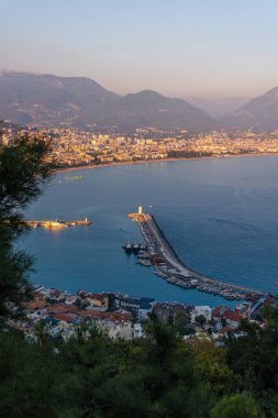 Akşamları Alanya (Türkiye) limanı. Binalar. Tekneleri ve gemileri olan körfez. Dağlar ve deniz. Dikey fotoğraf