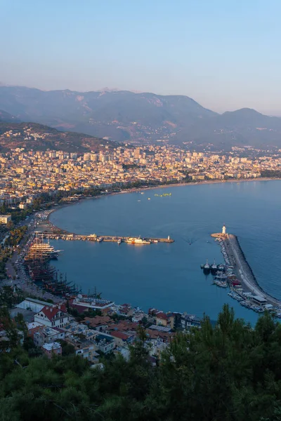 Akşamları Alanya (Türkiye) limanı. Binalar. Tekneleri ve gemileri olan körfez. Dağlar ve deniz. Dikey fotoğraf