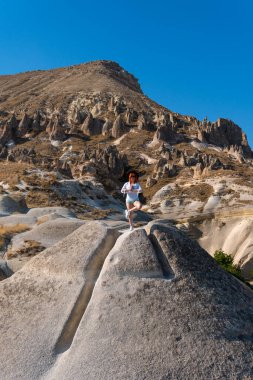 Gezgin kız, turist pozu, meditasyon, vyoga pozu. Arka planda peri bacaları var. Kaya oluşumları. Seyahat ve tatil, dikey fotoğraf. Goreme, Kapadokya, Türkiye turu.