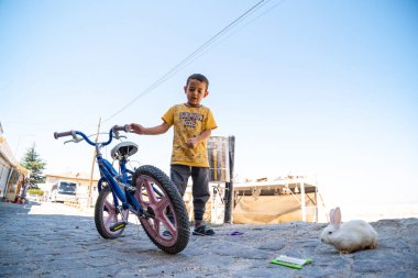 Uchisar, Türkiye - 27 Ağustos 2020: Buralı bir vatandaş, bisikletli bir çocuk, kirli küçük bir tavşanı olan kirli bir çocuk. yaşam standartları konsepti Kapadokya