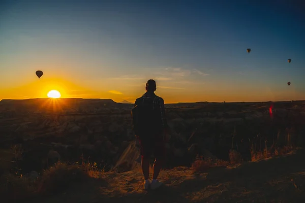 Back view silhouette. Man enjoy the sunrise. Tourist attraction balloon flight on background. Entertainment, tourism an vacation. Travel tour. Goreme, Cappadocia, Turkey.