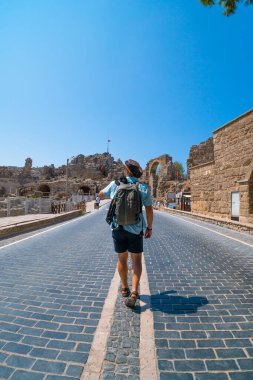 Sırt çantalı bir adam, gezgin şehrin harabelerine bakan antik Roma yolunda yürüyor. Türkiye 'de turizm ve turizm, Side. Dikey fotoğraf
