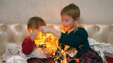 Çocuklar yatağa oturur, güzel bir kutudan Noel çelengi çıkarır ve onunla oynarlar. Işıklara bakıyorlar ve kabloları çözüyorlar. Bedenlerine bir çelenk asarlar.