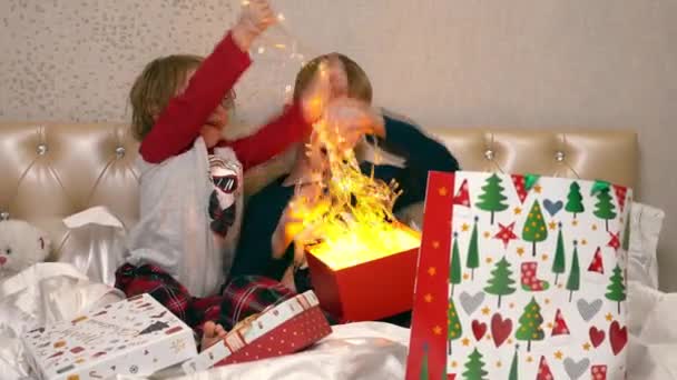 Kinderen zitten op het bed en halen een kerstslinger uit een mooie doos — Stockvideo