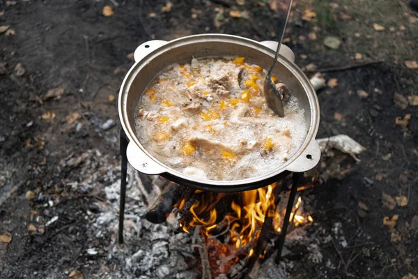 a cauldron with boiling chicken chowder made of chicken wings and vegetables stands on a fire during outdoor recreation. The soup is stirred with a long spoon