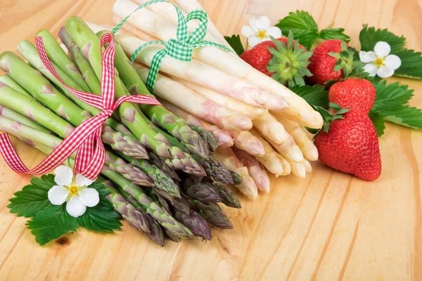 Bundel van verse asperges met aardbeien op hout. Veganistisch voedsel, vegetarisch en gezond koken concept. — Stockfoto