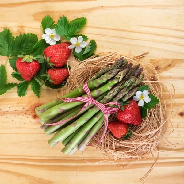 Grüner Spargel mit Erdbeeren. gesundes Gemüse über hellem Holz. Ansicht von oben. Stockbild