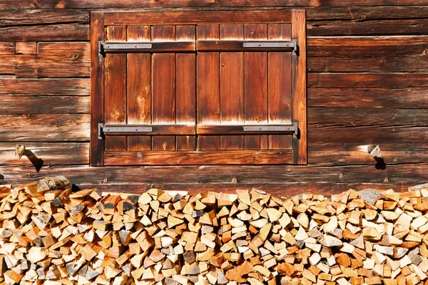 Closed window and stacked firewood of old alpine hut. Rural alpine scenery. — Stock Photo, Image