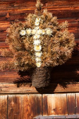 Retro decoration of a alpine hut, made from dry flowers in shape a cross. Outdoors image on a sunny day clipart