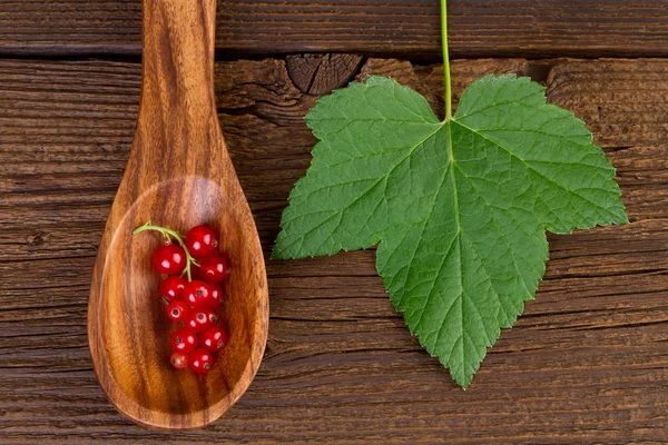 Grosella roja en cuchara de madera y hoja sobre fondo de madera — Foto de Stock