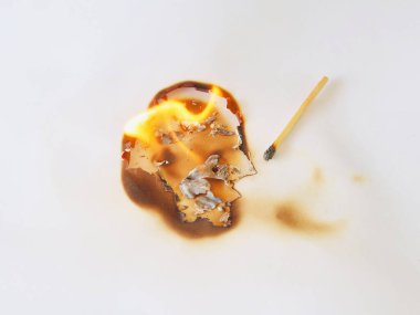 The image shows the paper being burned in a circular pattern, leaving dark brown burn marks on the white paper by a match.