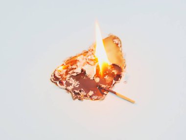 Close-up of burning paper and a burnt matchstick on a light background.