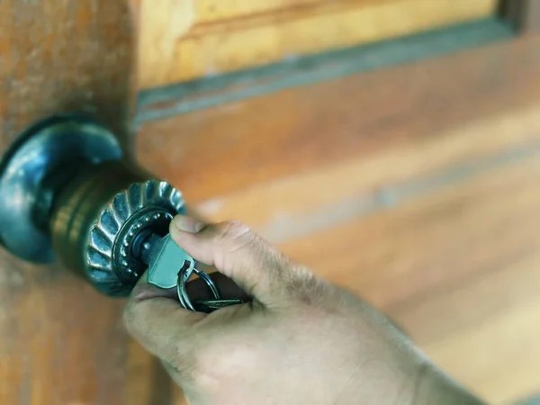 Koyu metal kapı tokmağını açmak için bir kişinin eli anahtar kullanır..