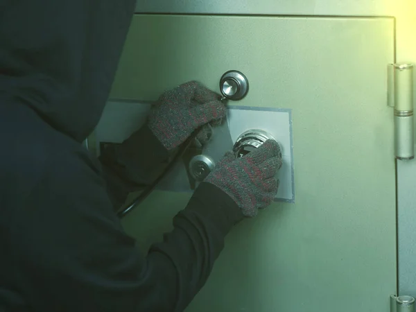 Eldiven ve koyu renk giysili bir hırsızın bir alet kullanarak bir kilidi açmaya ya da bir kasayı açmaya çalışması..