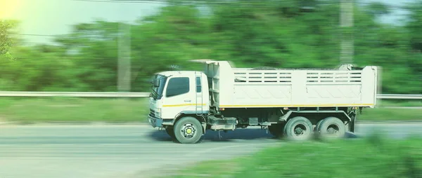 Beyaz bir çöp kamyonu asfalt yolda ilerliyor..