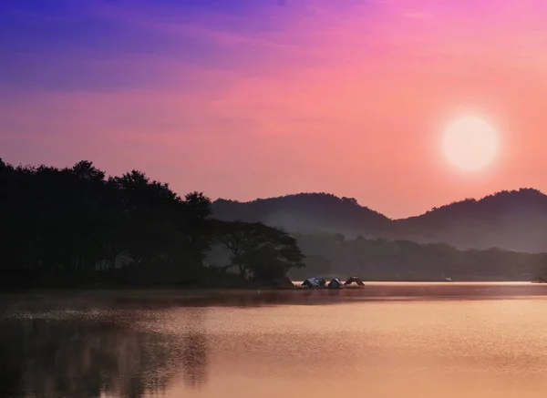 The image depicts a sunrise over water, with mountains and trees in the background.
