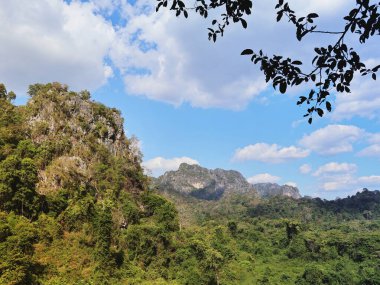 Bereketli kireçtaşı dağlarından oluşan yeşil ormanlarla kaplı parlak mavi bir gökyüzünün altında sürüklenen beyaz bulutlar..