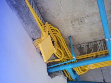 Bir inşaat alanının bitmemiş beton tavanında sarı elektrik kanalı ve mavi boruların kurulumunun detaylarını gösteren yakın çekim görüntüsü.