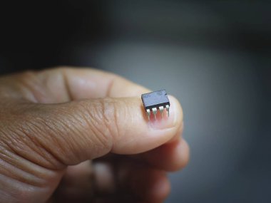 Bir yetişkinin başparmağı ile işaret parmağı arasına yerleştirilmiş siyah, 8-pin entegre devre (IC) çipinin yakın plan görüntüsü.