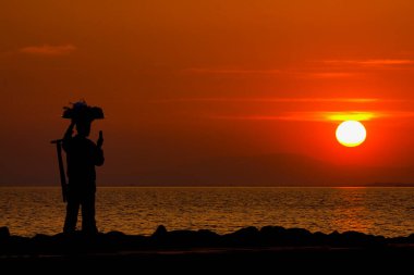 Midye satıcısı gün batımında deniz kenarında gün batımının fotoğrafını çekiyor. Siluetler.