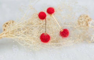 Kırmızı ponpon küpeler iki kabarık topa benzer. Küpelerin yanında rattan ürünleri ve buket örnekleri var. Bu eşyalar tülün üzerine yerleştiriliyor. Küpeler çok güzel ve şık görünüyor..