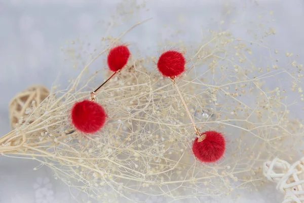 Kırmızı ponpon küpeler iki kabarık topa benzer. Küpelerin yanında rattan ürünleri ve buket örnekleri var. Bu eşyalar tülün üzerine yerleştiriliyor. Küpeler çok güzel ve şık görünüyor..