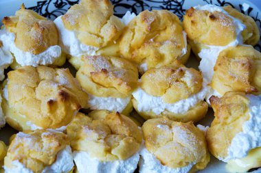 Sarı vanilya kremalı lezzetli prenses çörekleri ve beyaz arka plandaki tepside çırpılmış krema.