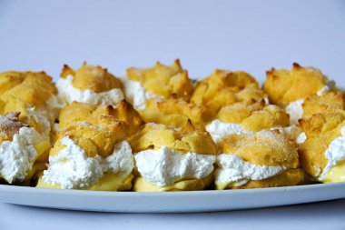 Sarı vanilya kremalı lezzetli prenses çörekleri ve beyaz arka plandaki tepside çırpılmış krema.