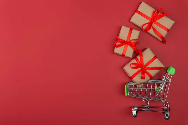 Caja de regalo con cinta roja en mini carrito de comestibles sobre fondo rosa — Foto de Stock